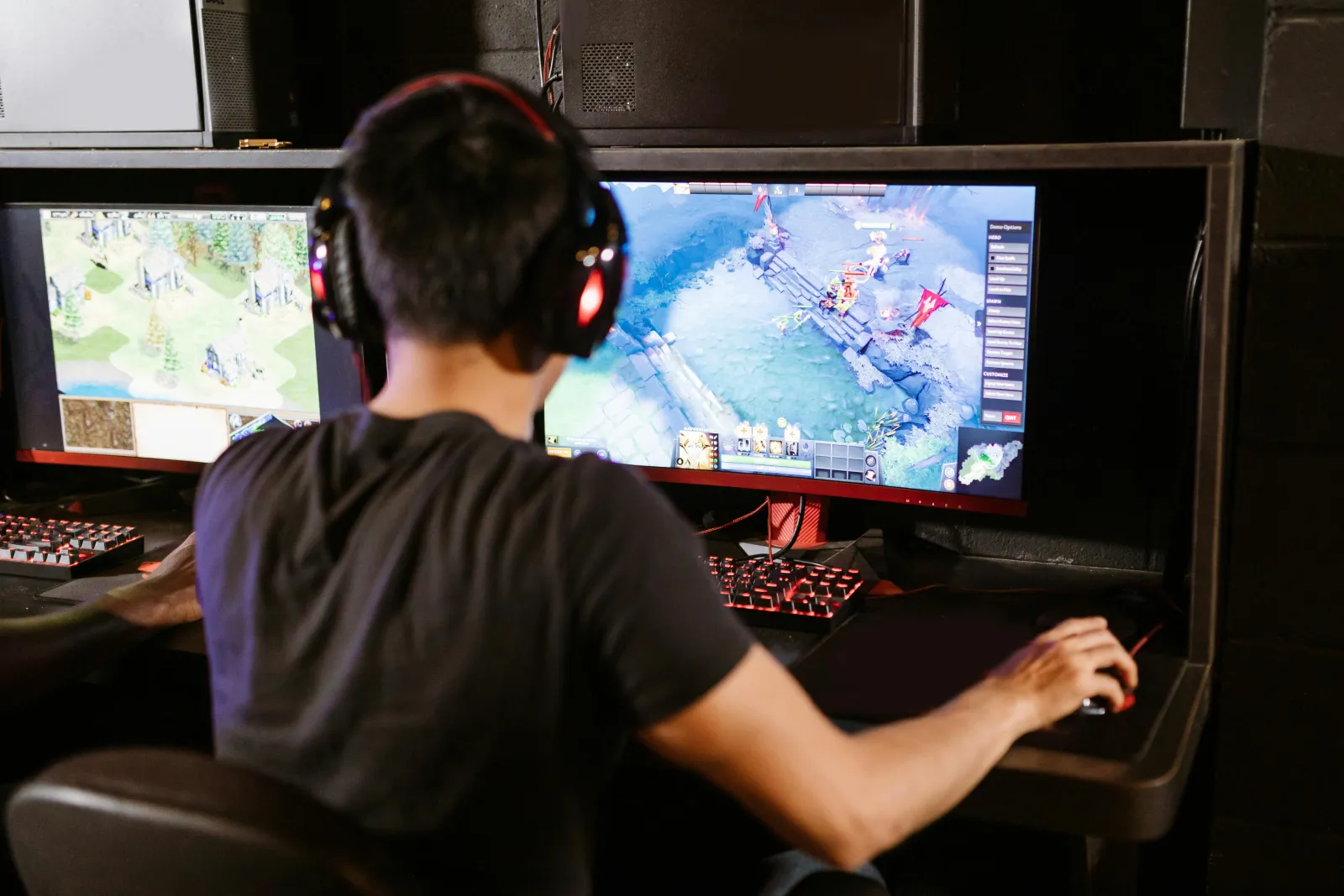 Person at a gaming setup, two wide monitors, RGB-lit keyboard, headphones on